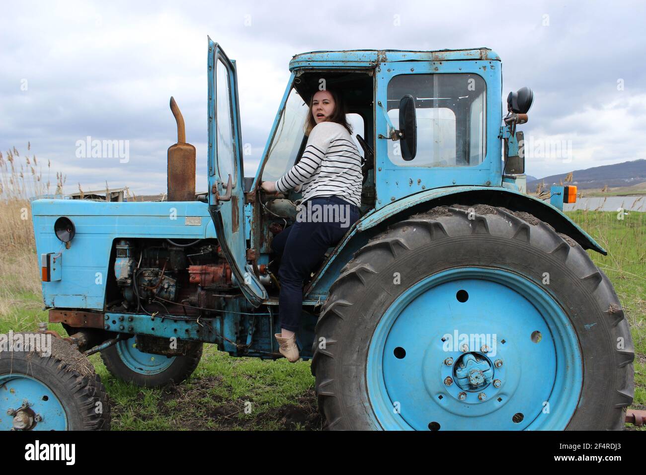 La ragazza sul trattore nel campo. Arare il terreno del trattore in autunno. Lavori agricoli. Foto Stock