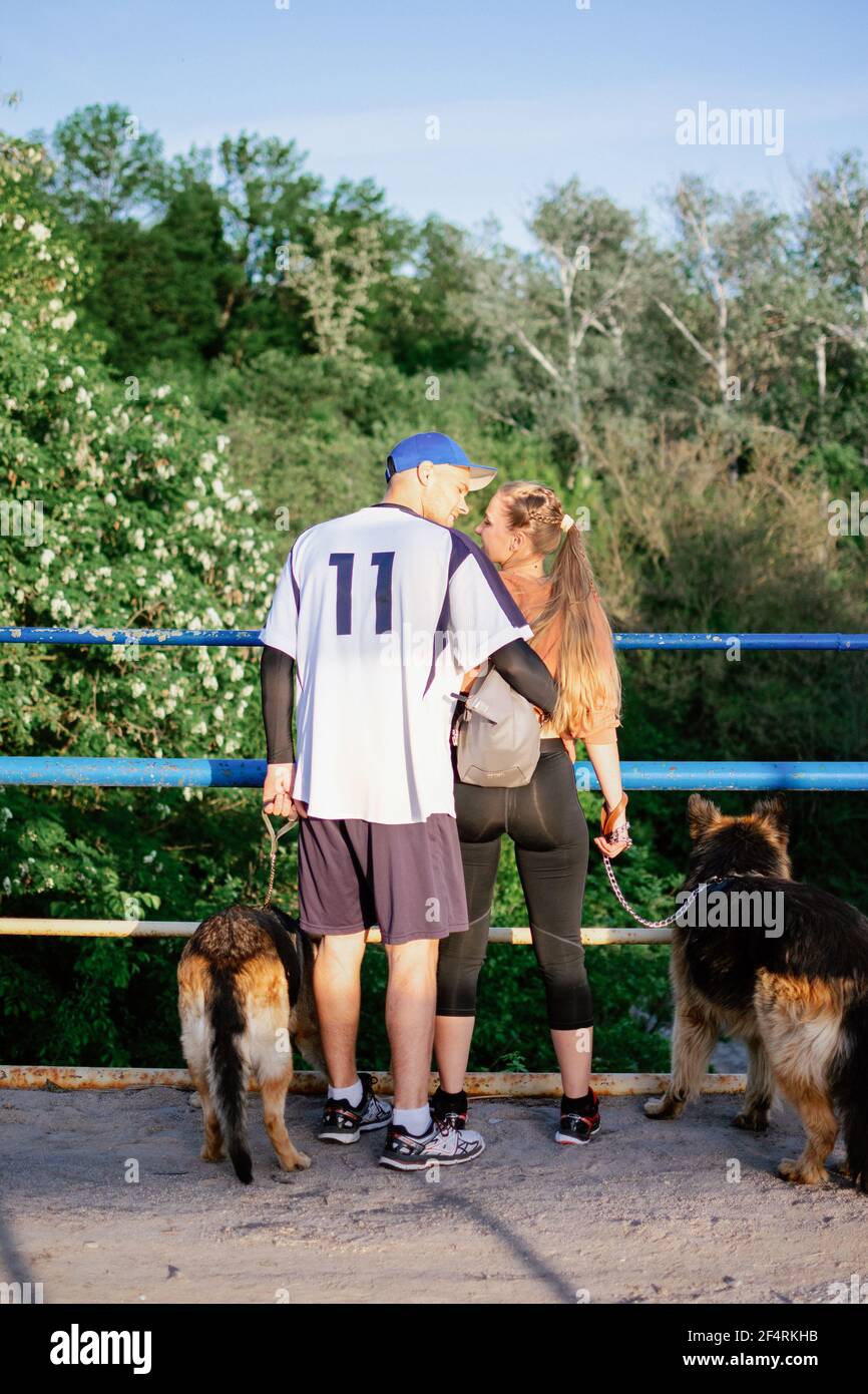 Famiglia attiva, coppia di fitness, amore dell'animale domestico, addestramento del cane, razze del cane migliori per la famiglia. Giovane coppia sportiva che cammina con due cani da pastore tedeschi all'aperto Foto Stock
