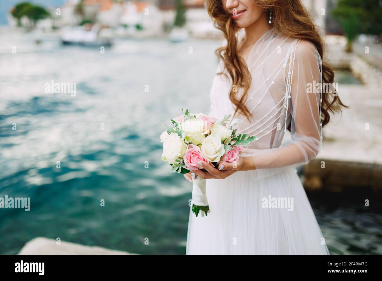 La sposa tiene in mano un bouquet di rose e si trova sul molo vicino alla città vecchia di Perast Foto Stock