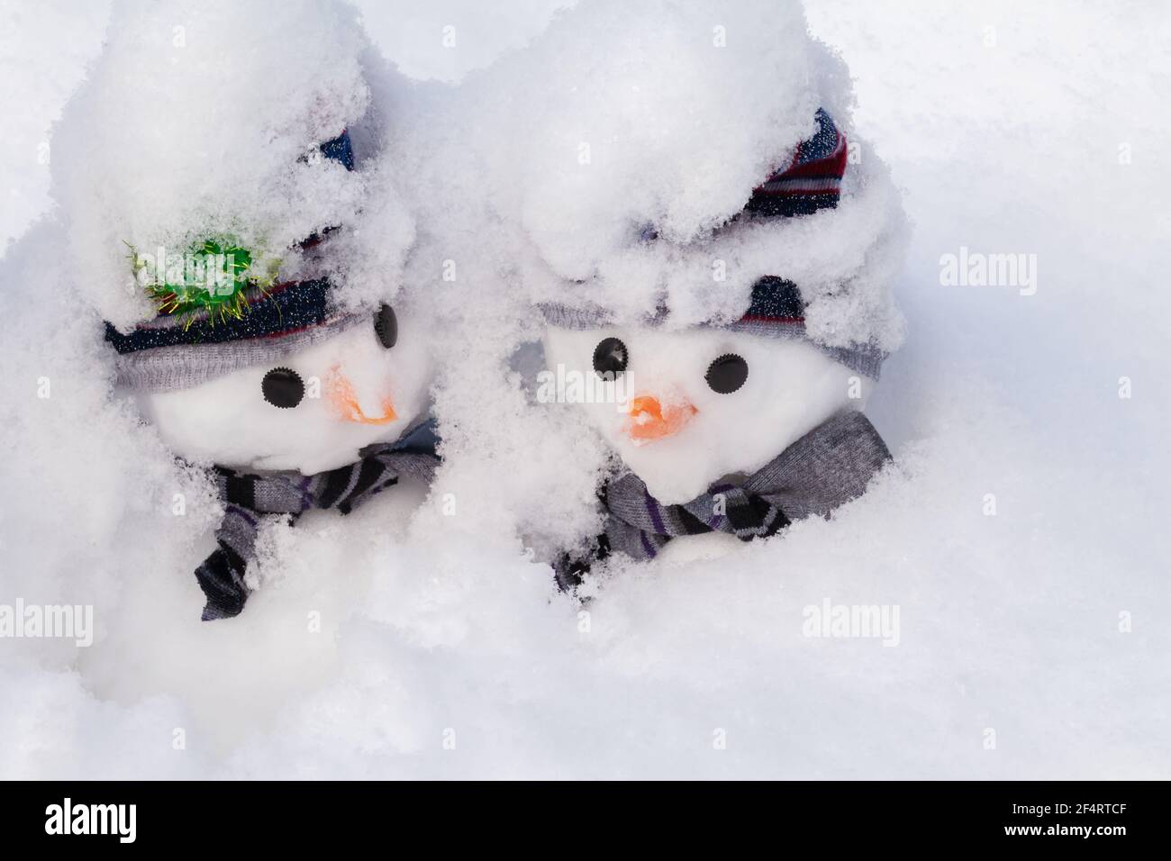 Due piccoli pupazzi di neve sepolti in profondità in una caduta di neve degli inverni. Personaggi carini per il divertimento natalizio e l'umorismo indossando cappelli e sciarpe Foto Stock