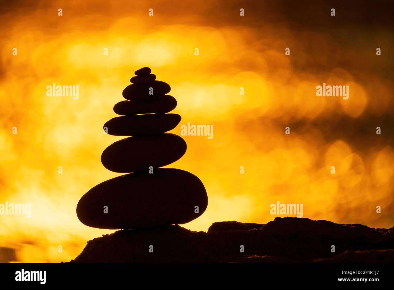 Profilo a piramide di ciottoli bilanciato sulla spiaggia. Astratto caldo tramonto bokeh con Mare sullo sfondo. Pietre Zen sulla spiaggia di mare, meditazione, spa Foto Stock