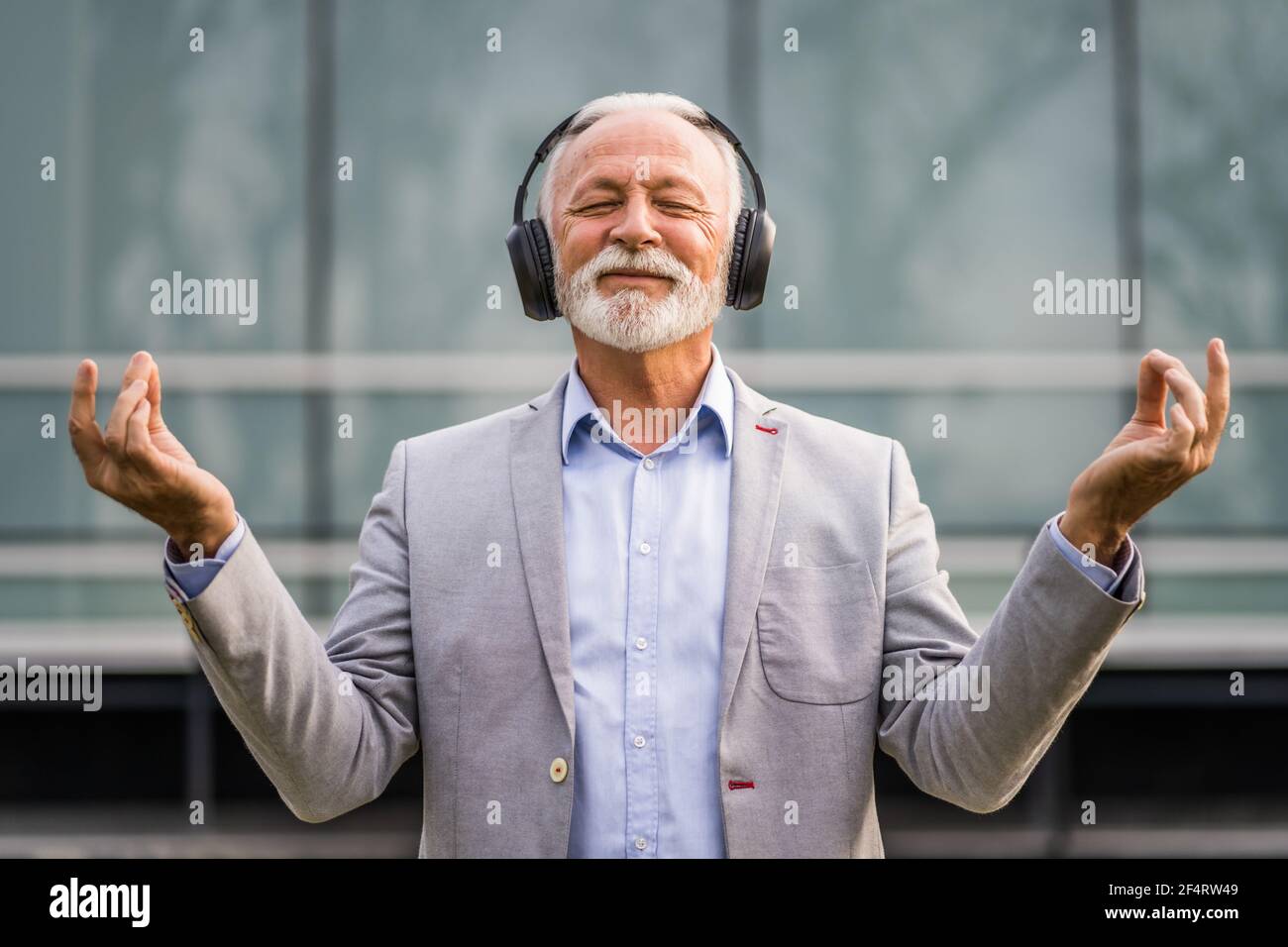 Ritratto all'aperto di un uomo d'affari anziano che sta godendo la musica sulle cuffie e meditando. Foto Stock
