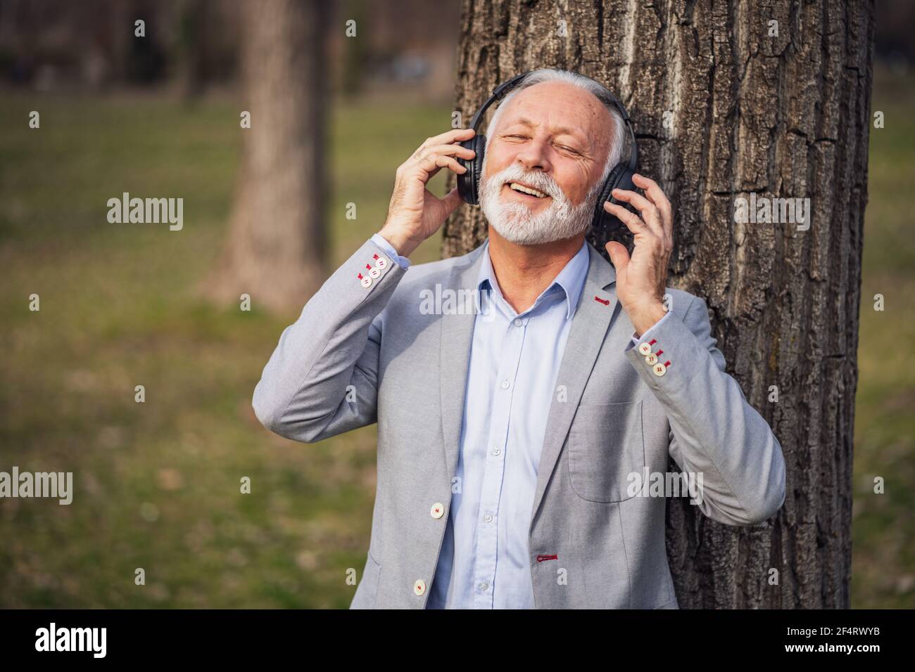 Ritratto esterno di uomo d'affari senior che si rilassa nel parco. Sta ascoltando musica con le cuffie. Foto Stock