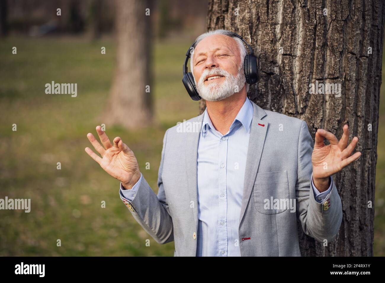 Ritratto esterno di uomo d'affari senior che si rilassa nel parco. Sta ascoltando musica con le cuffie. Foto Stock