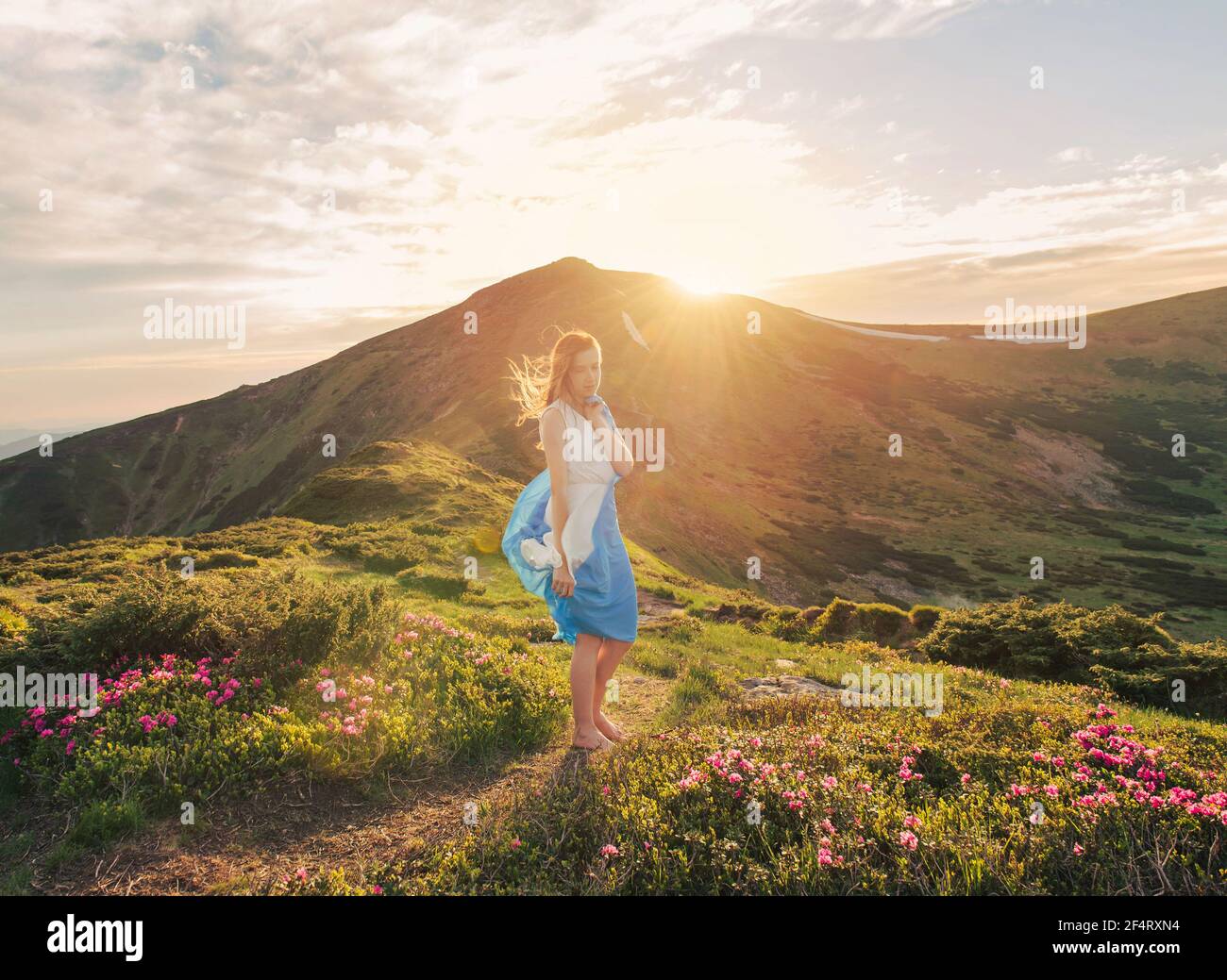 La donna sente la libertà e gode della natura in montagna con tessuto blu in mani al tramonto Foto Stock