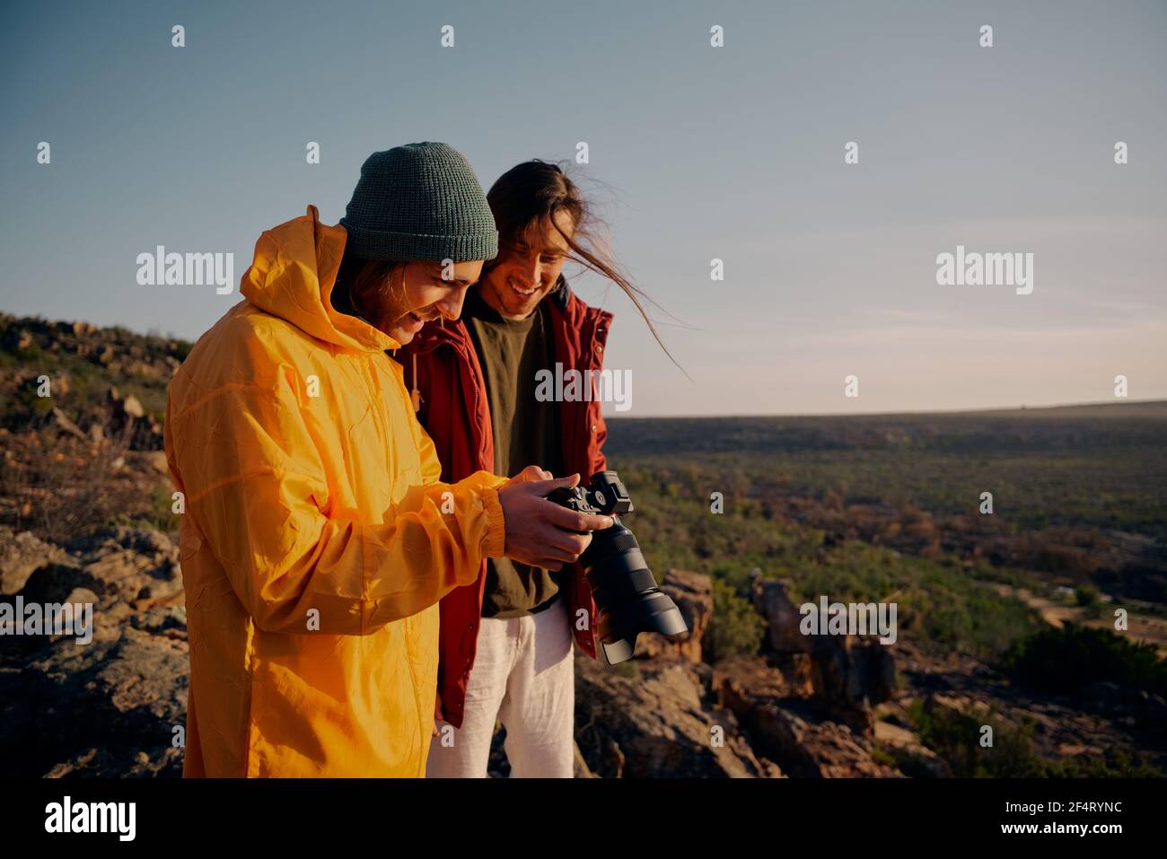 Felici amici maschi che guardano la fotocamera dopo aver fotografato la fotocamera perfetta scatto di alba sulla scogliera di montagna Foto Stock
