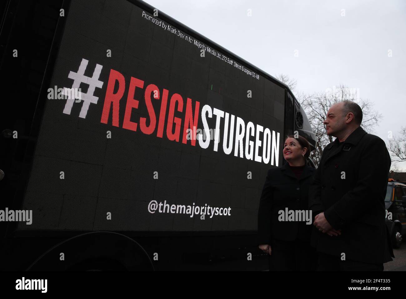 Mark e Mary Devlin guardano a un tabellone mobile che hanno organizzato e che dice "ResignSturgeon" mentre guida attraverso la circoscrizione del primo ministro Nicola Sturgeon nella zona di Govanhill a Glasgow come parte della campagna di ResignSturgeon della maggioranza in vista delle elezioni scozzesi del 6 maggio. Data immagine: Martedì 23 marzo 2021. Foto Stock