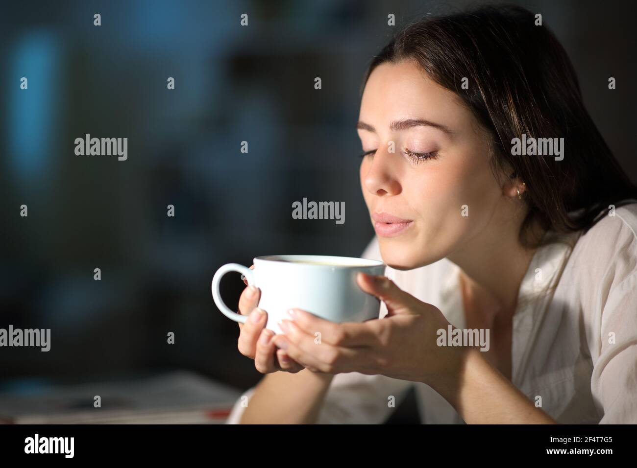 Donna che soffia per raffreddare il caffè caldo di notte il soggiorno a casa Foto Stock