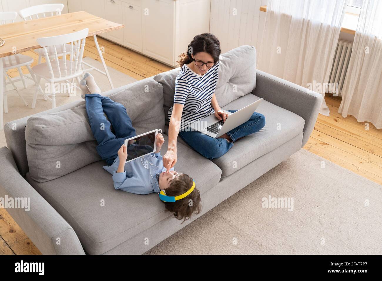 MOM freelance lavoro remoto da casa ufficio su computer portatile sedersi sul divano bambino giocare su tablet. Blocco Foto Stock