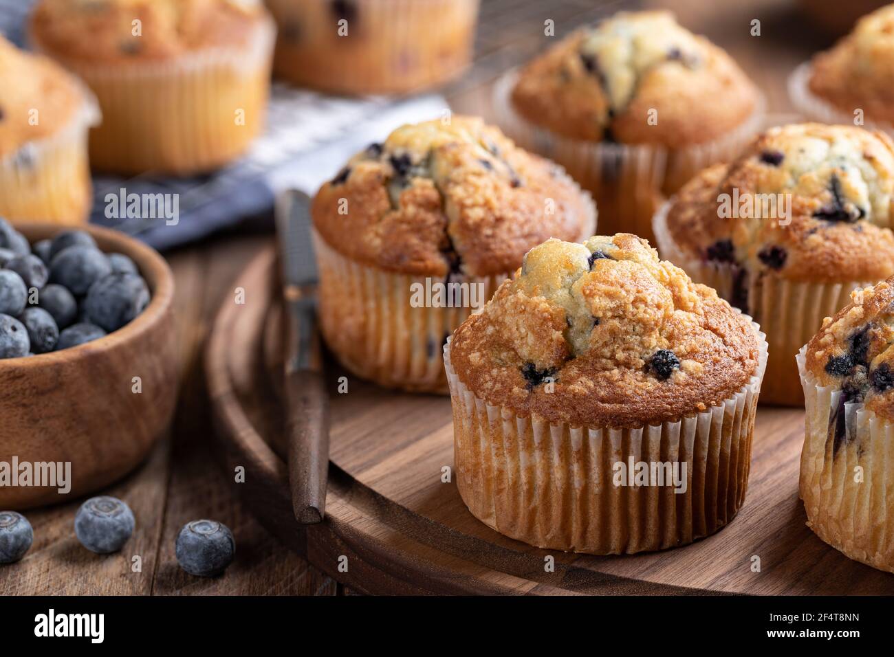 Muffin ai mirtilli su un piatto di legno con frutti di bosco e muffin in background Foto Stock