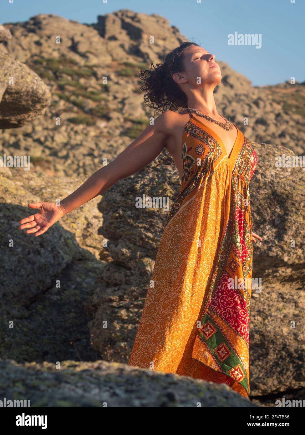 Donna in abito arancione che pratica yoga al tramonto. Foto Stock