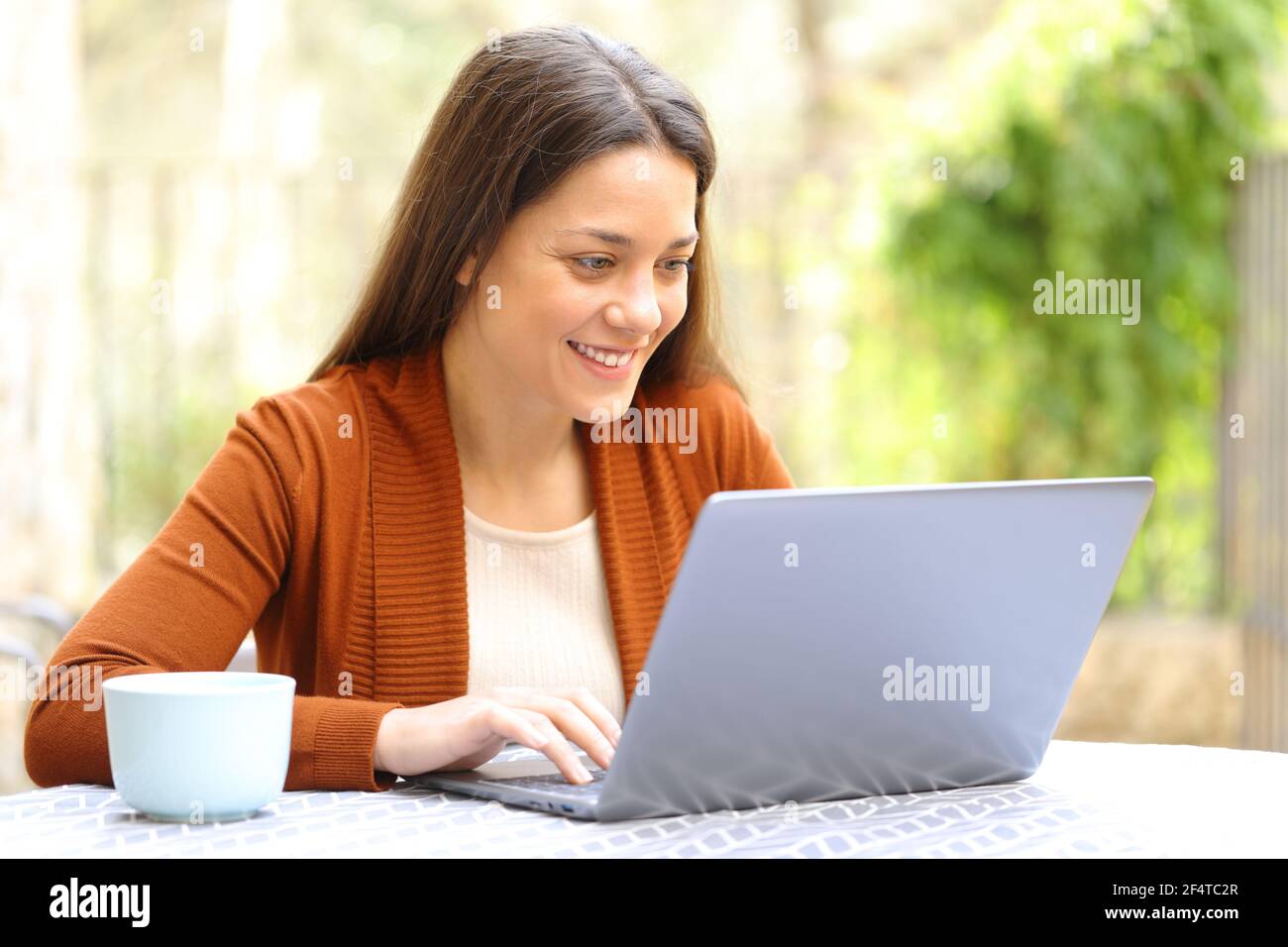 Donna felice che naviga i contenuti del computer portatile all'aperto in una terrazza della casa Foto Stock