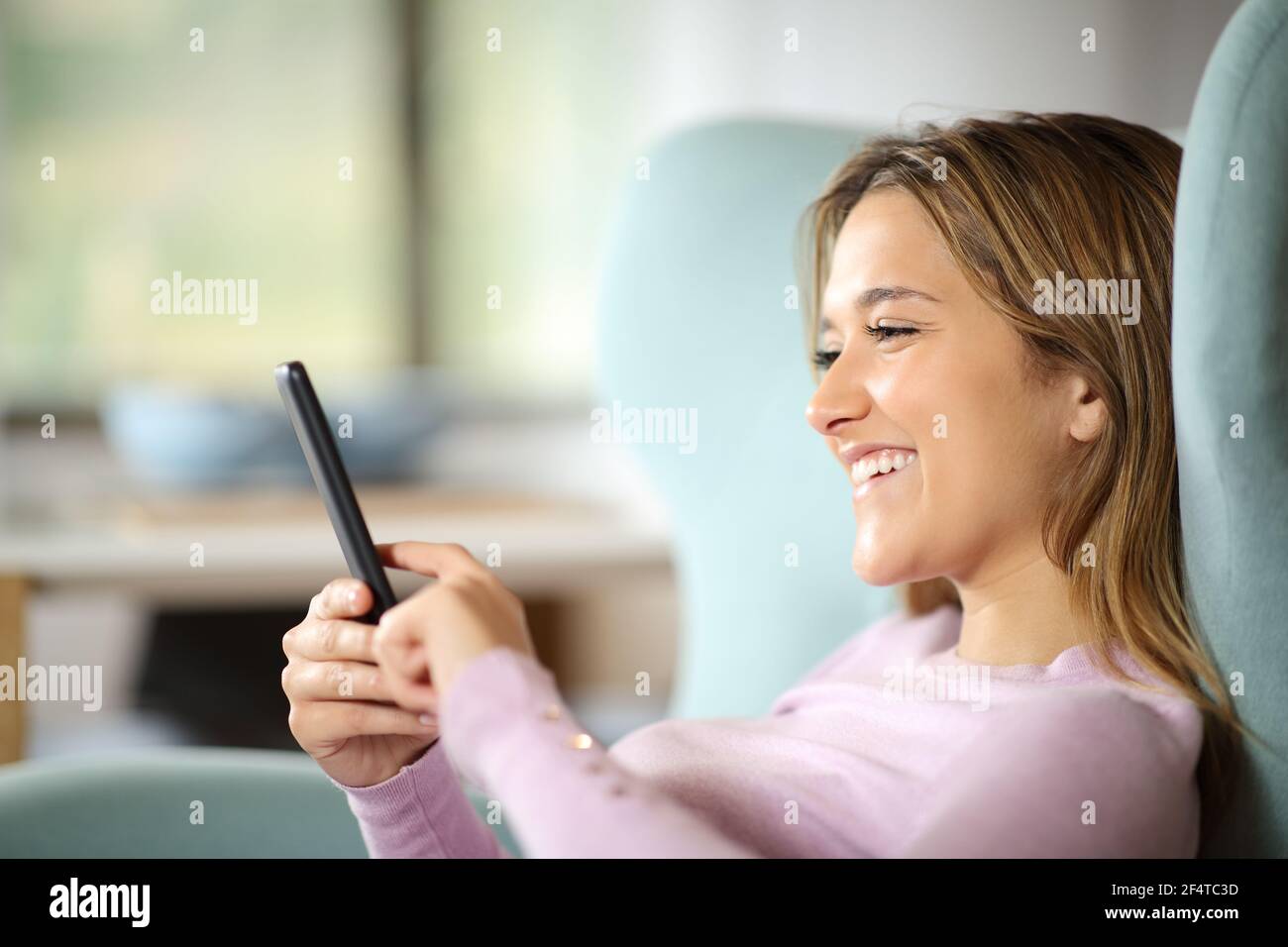 Donna felice che controlla il contenuto dello smartphone seduto su un divano a casa Foto Stock