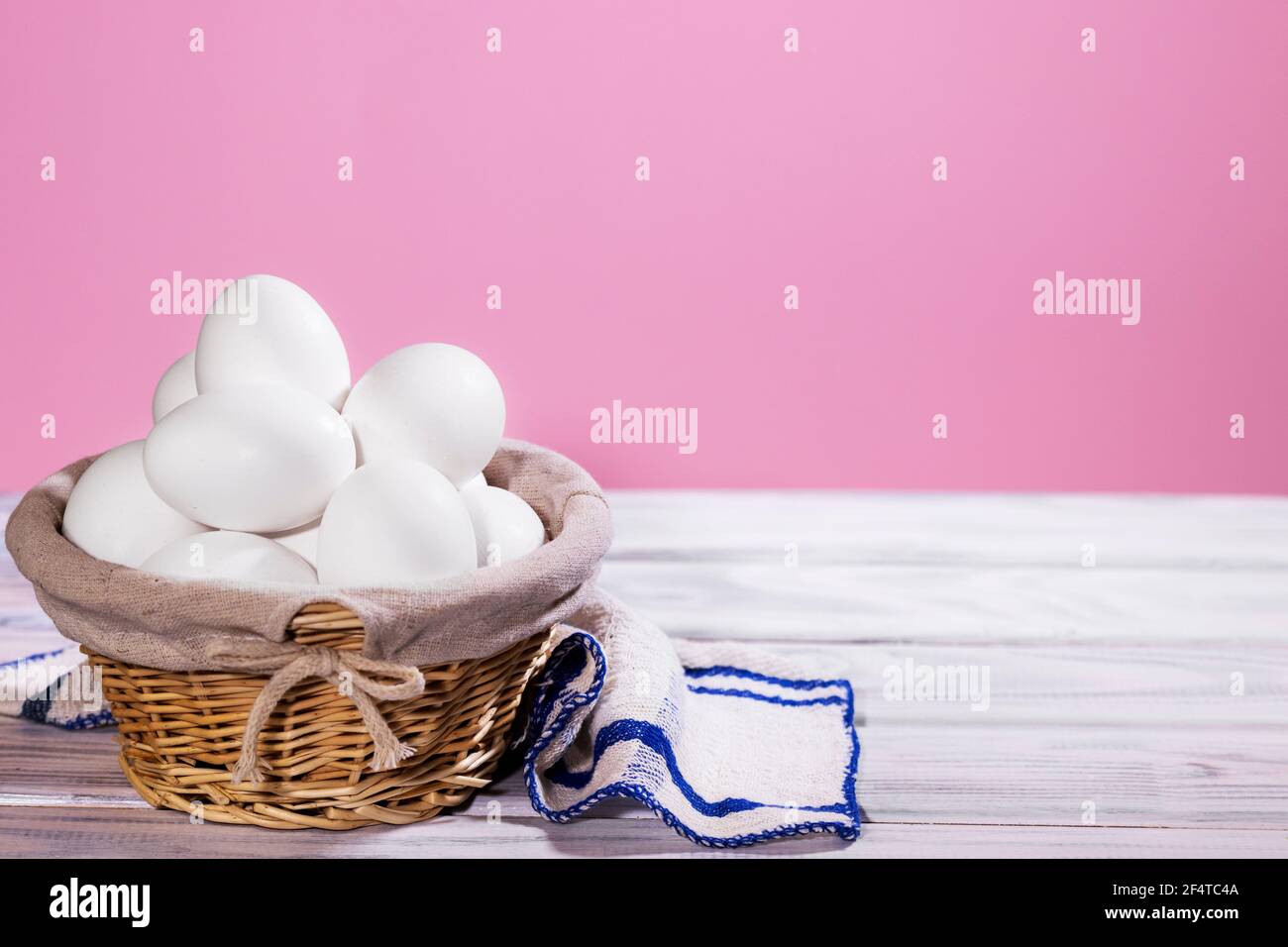 Uova di pollo bianche in un cestino di paglia su uno sfondo rosa con pezzo di stoffa, prodotto naturale Foto Stock