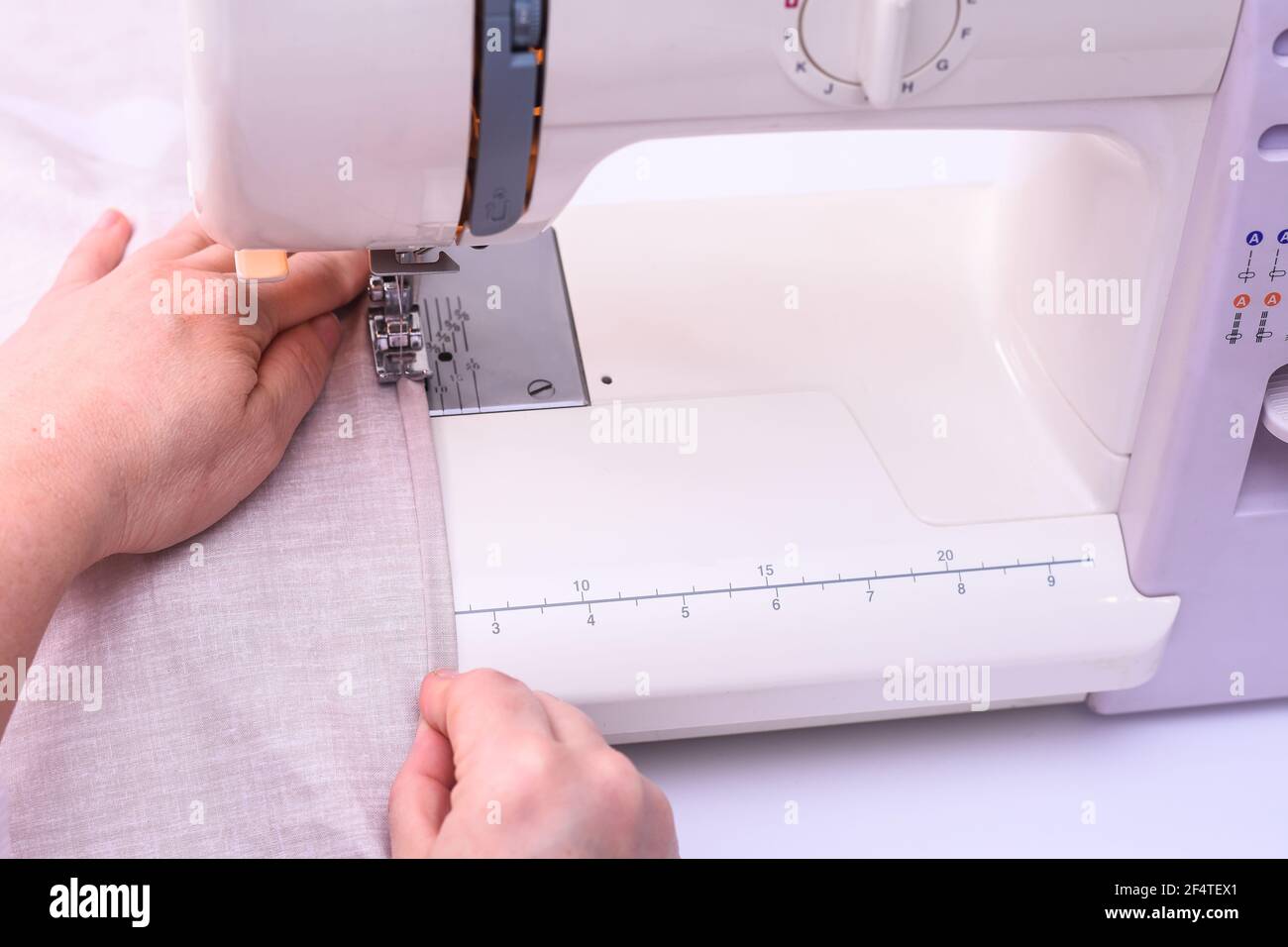 Le mani femminili cucire il tessuto leggero sulla macchina da cucire a casa. Foto Stock