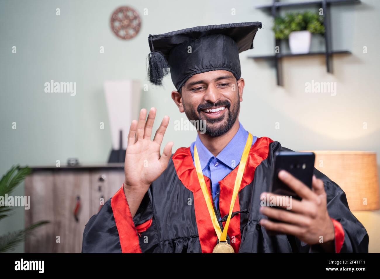 Studente che frequenta la sua cerimonia di laurea video online dal telefono cellulare in abito di laurea - concetto di celebrazioni virtuali, nuovo normale durante Foto Stock