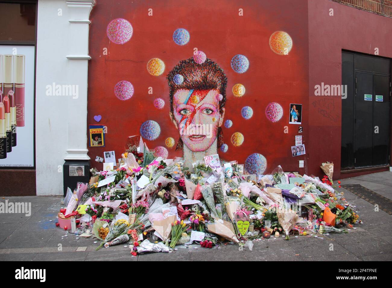 LONDRA, UK - GENNAIO 12 2016: Fiori posati dai fan di David Bowie al murale del musicista a Brixton dopo la sua morte Foto Stock