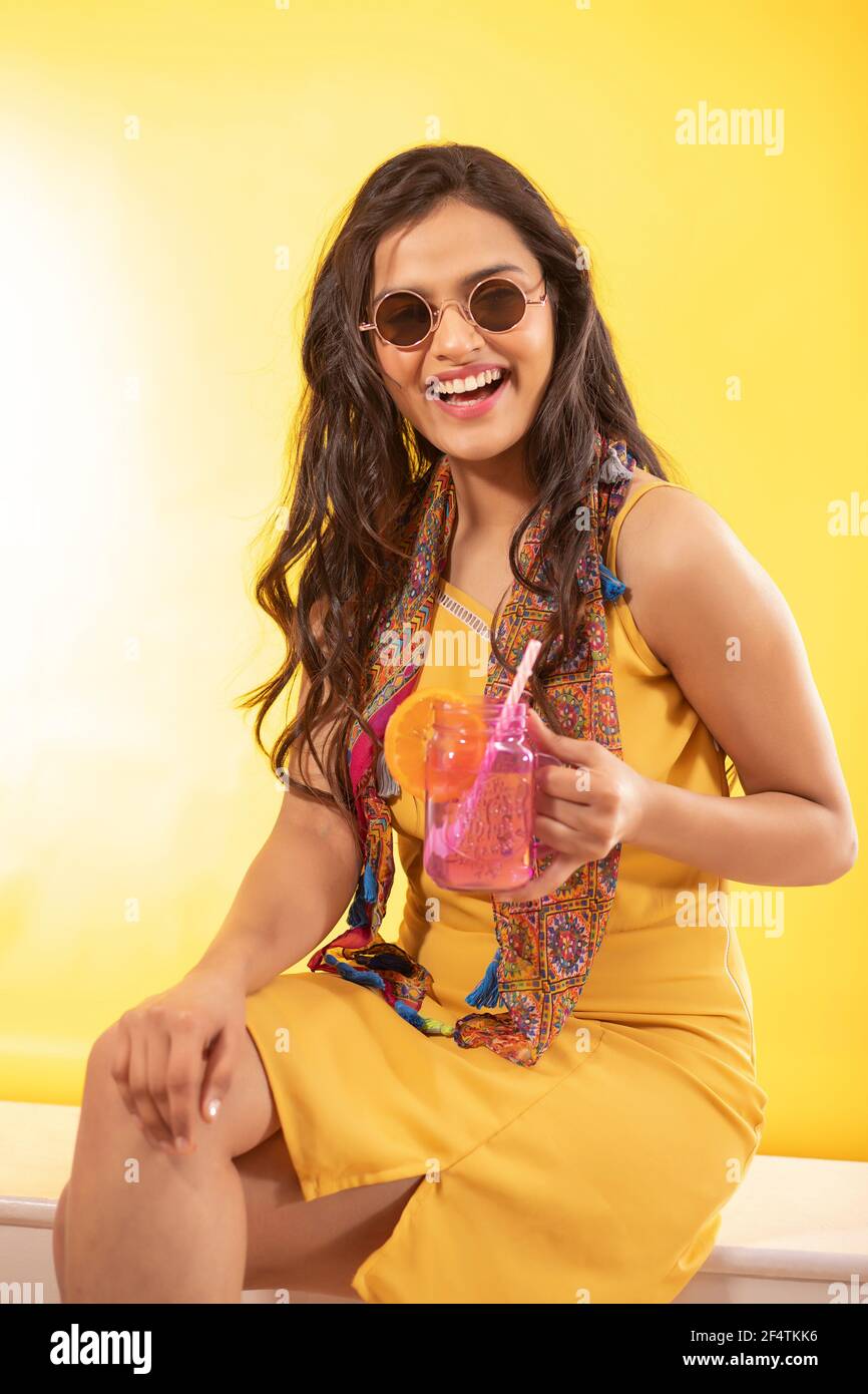 UNA GIOVANE DONNA ALLA MODA CHE RIDE MENTRE SI SIEDE CON UN DRINK IN MANO Foto Stock