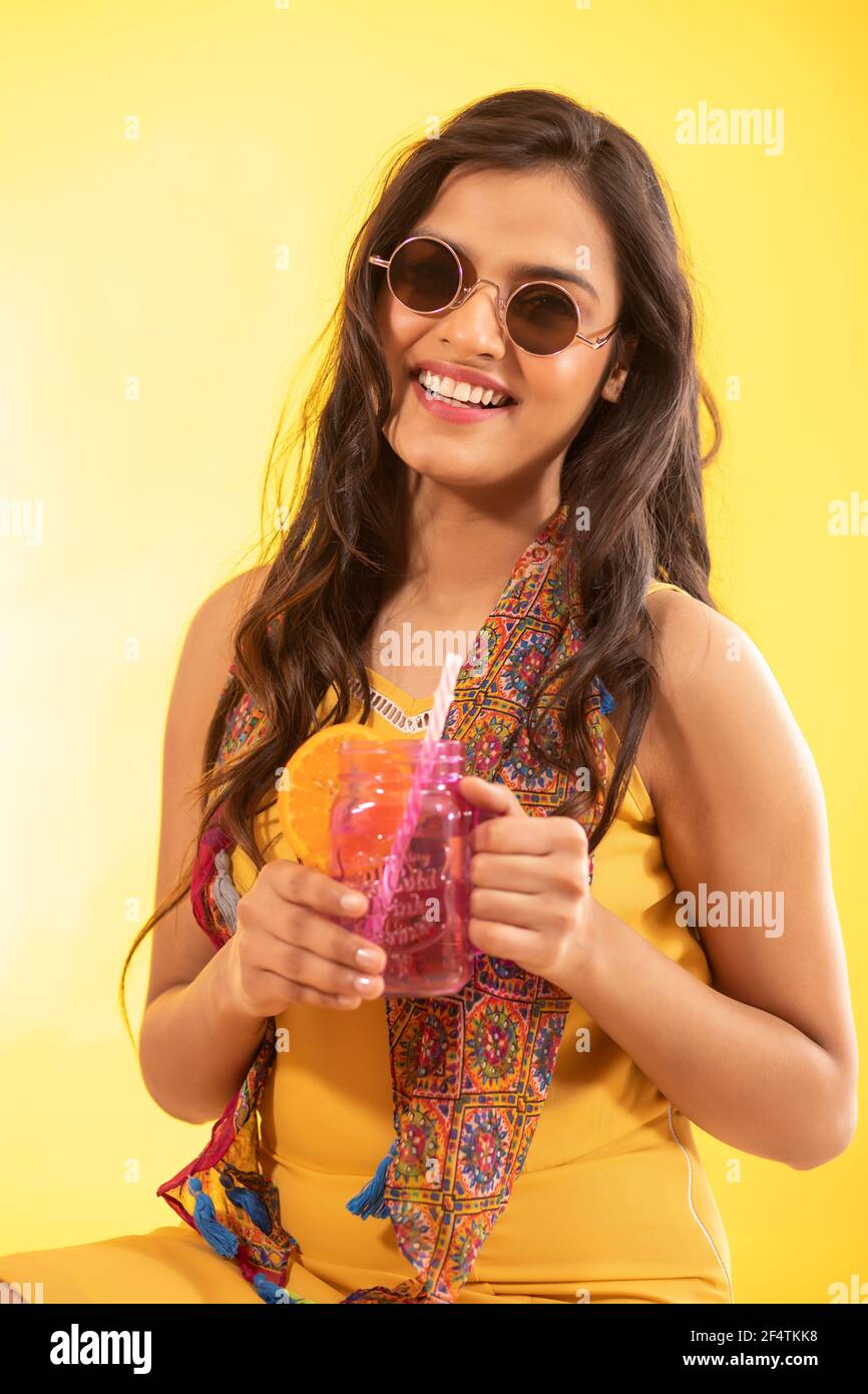 UNA GIOVANE DONNA ALLEGRA IN POSA DAVANTI ALLA MACCHINA FOTOGRAFICA CON BEVANDA DI FRUTTA IN MANO Foto Stock