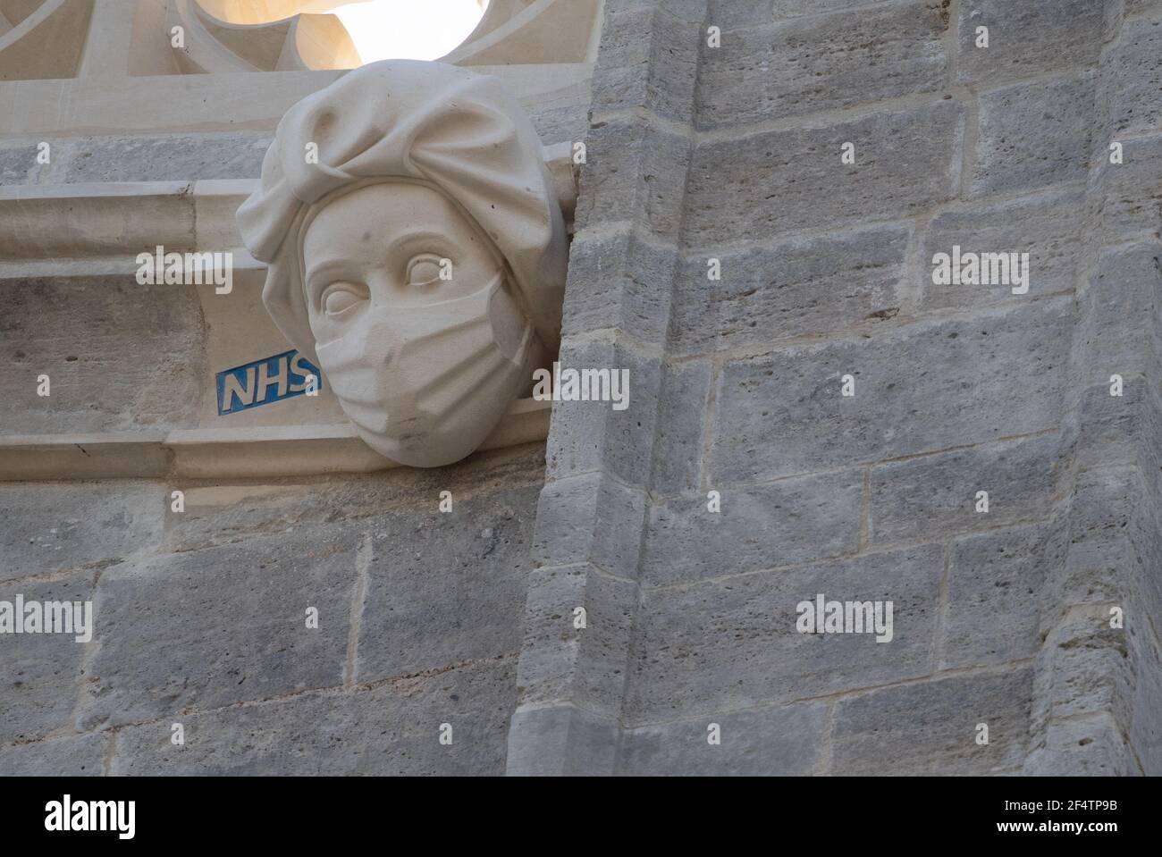 Un'incisione di un operaio NHS indossante maschera sul lato del Priorato di Christchurch in Dorset durante il terzo blocco nazionale dell'Inghilterra per frenare la diffusione del coronavirus. La scultura è un tributo permanente agli sforzi del servizio sanitario durante la pandemia ed è stata aggiunta al Priorato - la cui storia risale alla metà del 11 ° secolo - come parte di un progetto per sostituire i gargoyle danneggiati e grottesche. Data immagine: Martedì 23 marzo 2021. Foto Stock