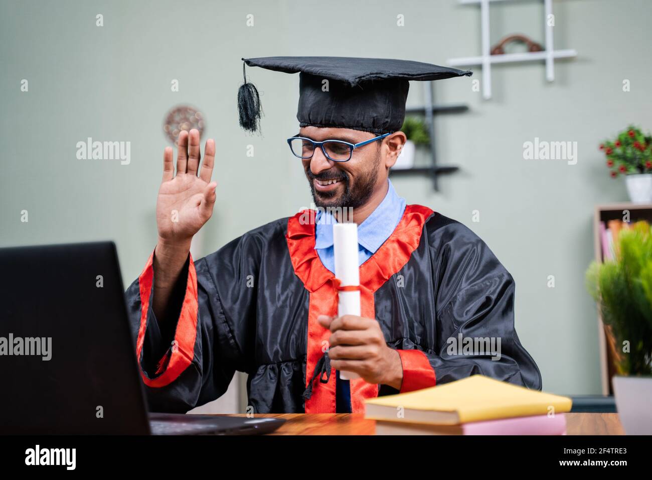 Studente che frequenta una laurea virtuale dal computer portatile con certificato di laurea in abito da casa - concetto di celebrazioni virtuali, nuova normalità Foto Stock