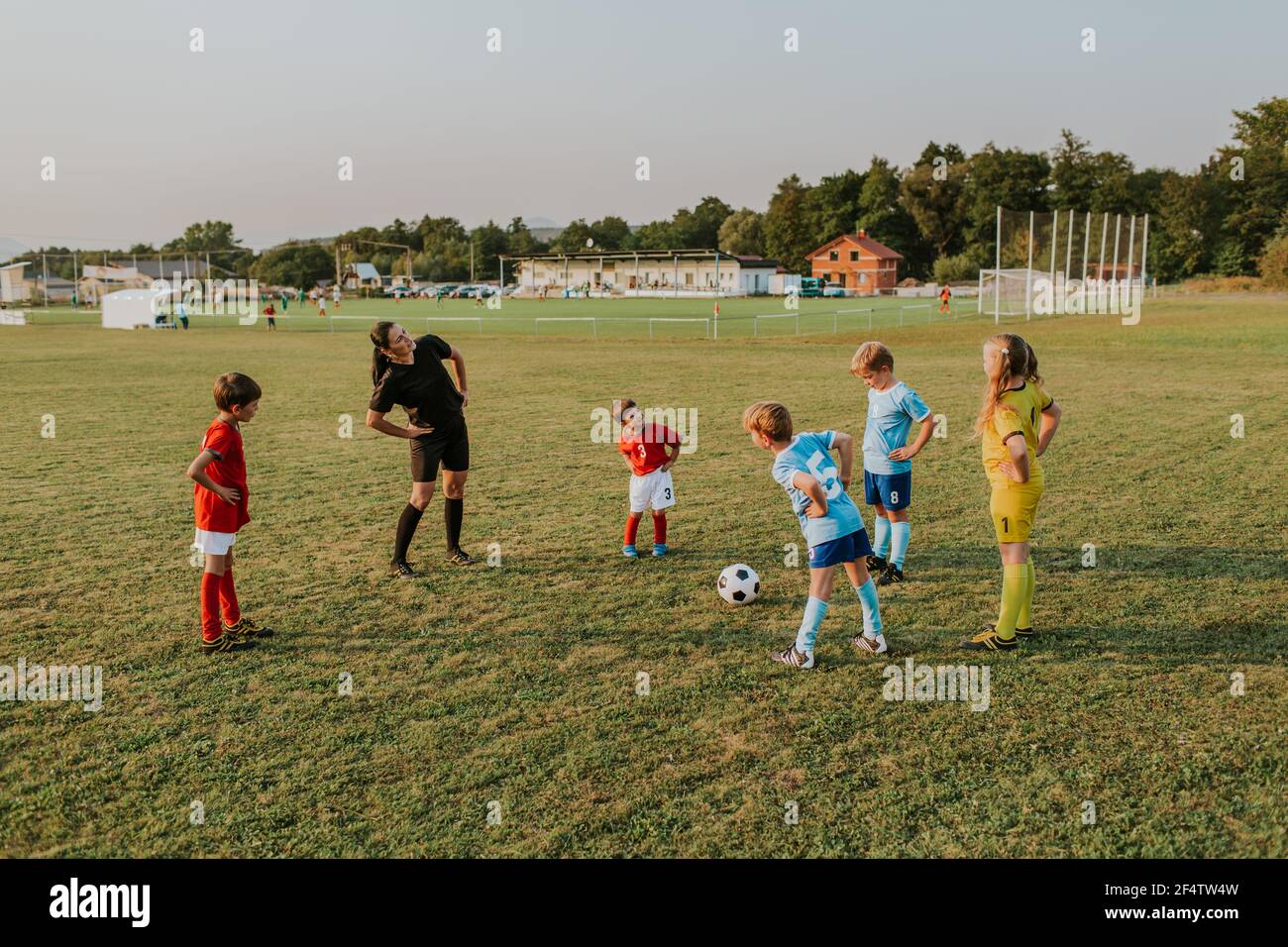 I bambini si riscaldano prima dell'allenamento. Gruppo di bambini che si allungano insieme con la loro allenatrice femminile prima di giocare a calcio in campo al tramonto. Foto Stock