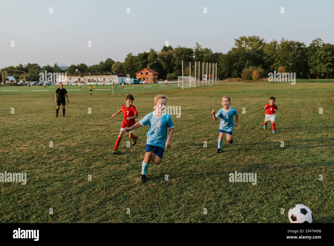 Bambini che giocano a calcio amatoriale. Ragazzi allegri che corrono dopo la palla di calcio fuori sul campo al tramonto. Foto Stock