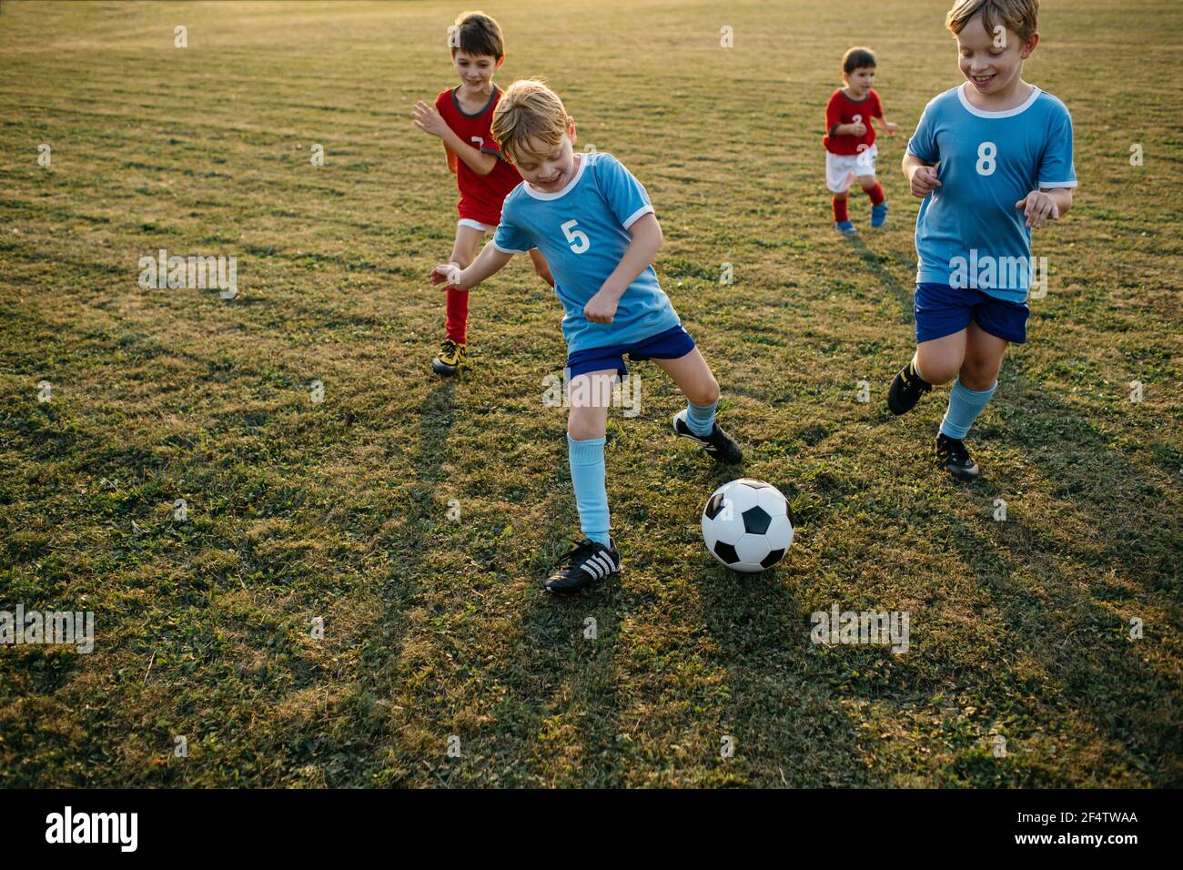 Bambini che giocano a calcio amatoriale. Ragazzi allegri che corrono dopo la palla di calcio fuori sul campo al tramonto. Foto Stock