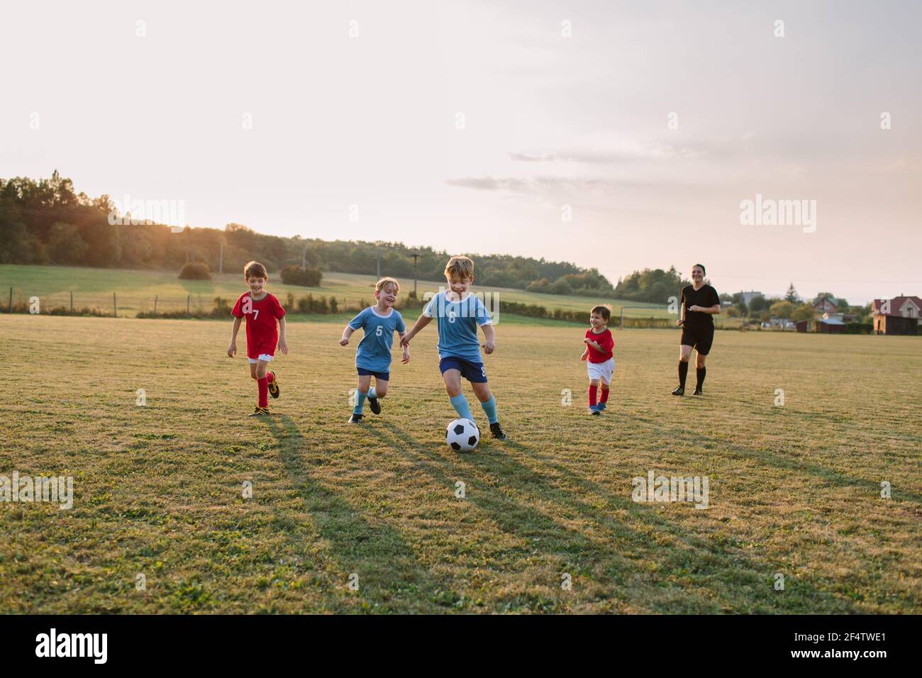 Bambini che giocano a calcio. Tutta la lunghezza dei ragazzi allegri in abiti da calcio che inseguono la palla sul campo. Foto Stock