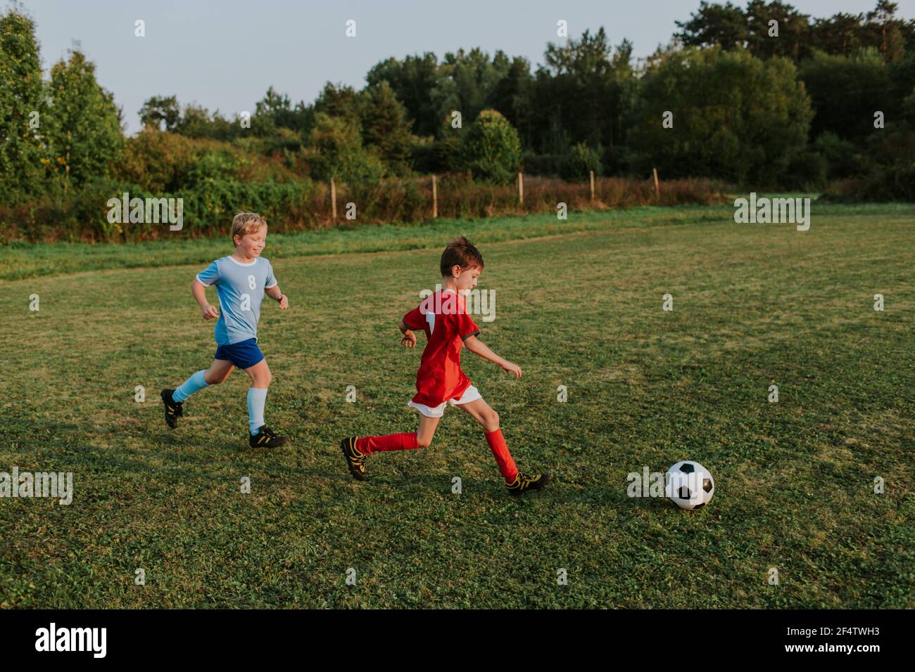 Bambini che corrono dopo la palla di calcio. Una lunghezza completa di ragazzi allegri in abiti da calcio che inseguono la palla sul campo da calcio. Foto Stock