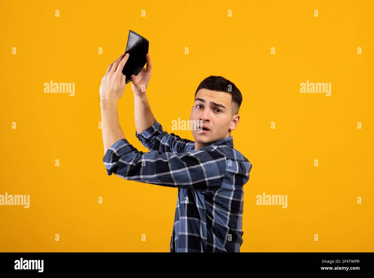 Uomo millenario infelice scuotendo portafoglio vuoto su sfondo studio arancione Foto Stock
