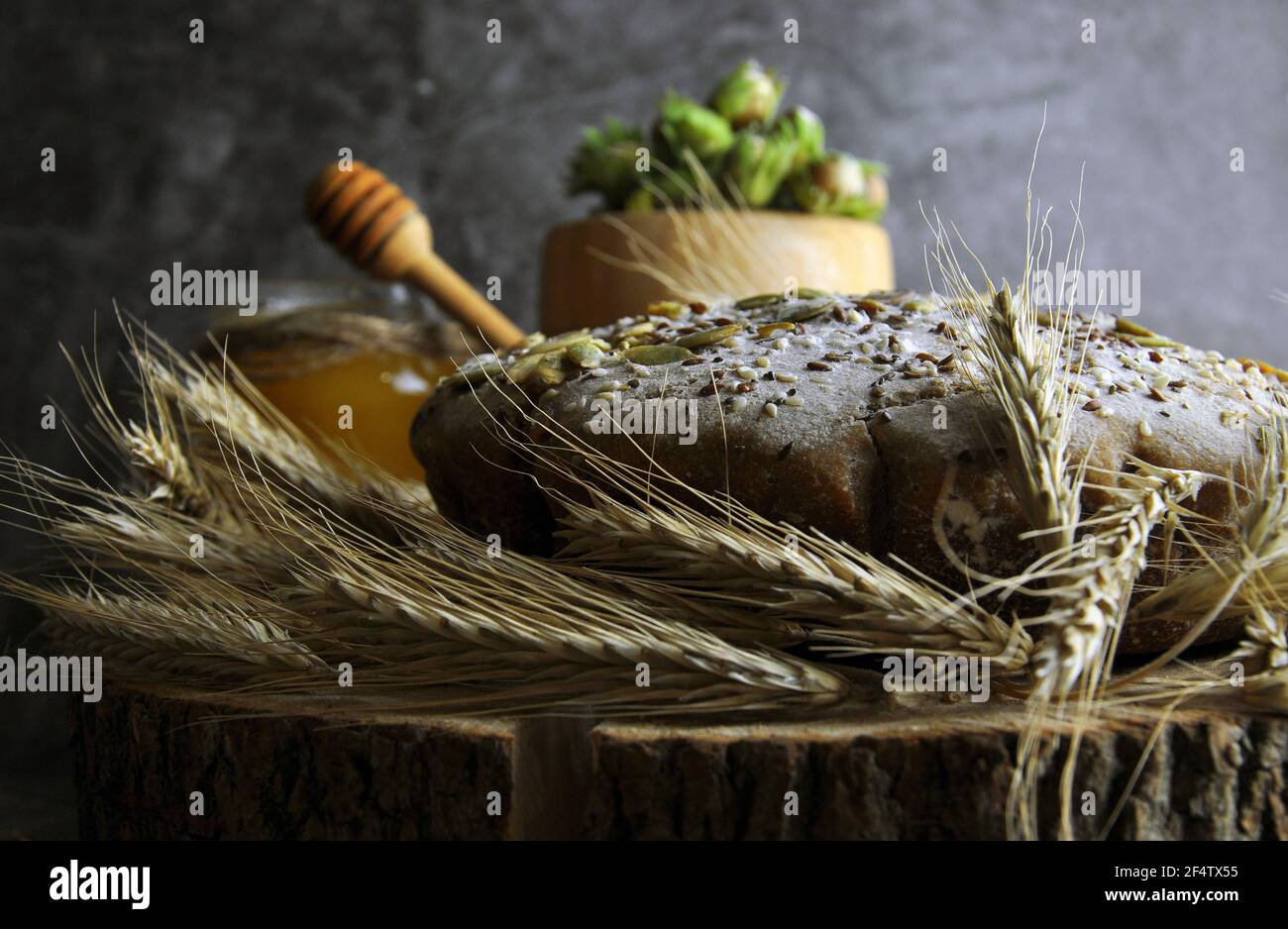Pane di grano intero su una tavola di legno primo piano. Vista laterale. Miele e una ciotola di noci sullo sfondo. Foto Stock