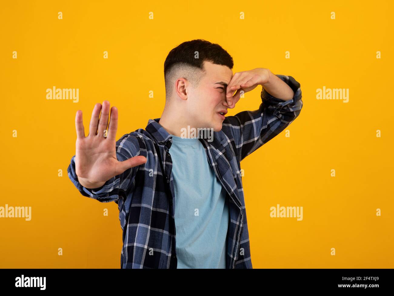 Giovane caucasico che chiude il naso, soffrendo di cattivo odore, gesturing STOP su sfondo arancione studio Foto Stock