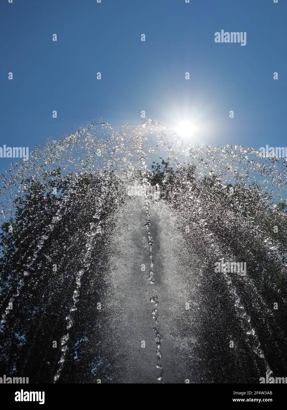 Il sole illumina il getto della fontana che spriggerà verso l'alto sullo sfondo del cielo blu Foto Stock