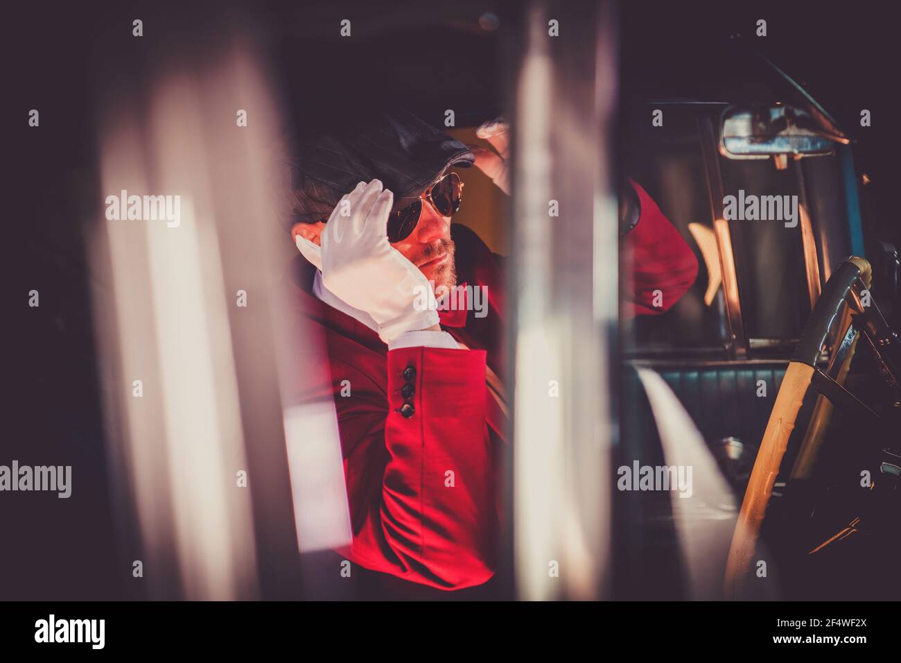 Elegante vintage cercando uomini caucasici nella sua auto classica di guida anni '30. Controllare il cappello nello specchietto retrovisore interno dell'auto. Tema automobilistico classico. Foto Stock