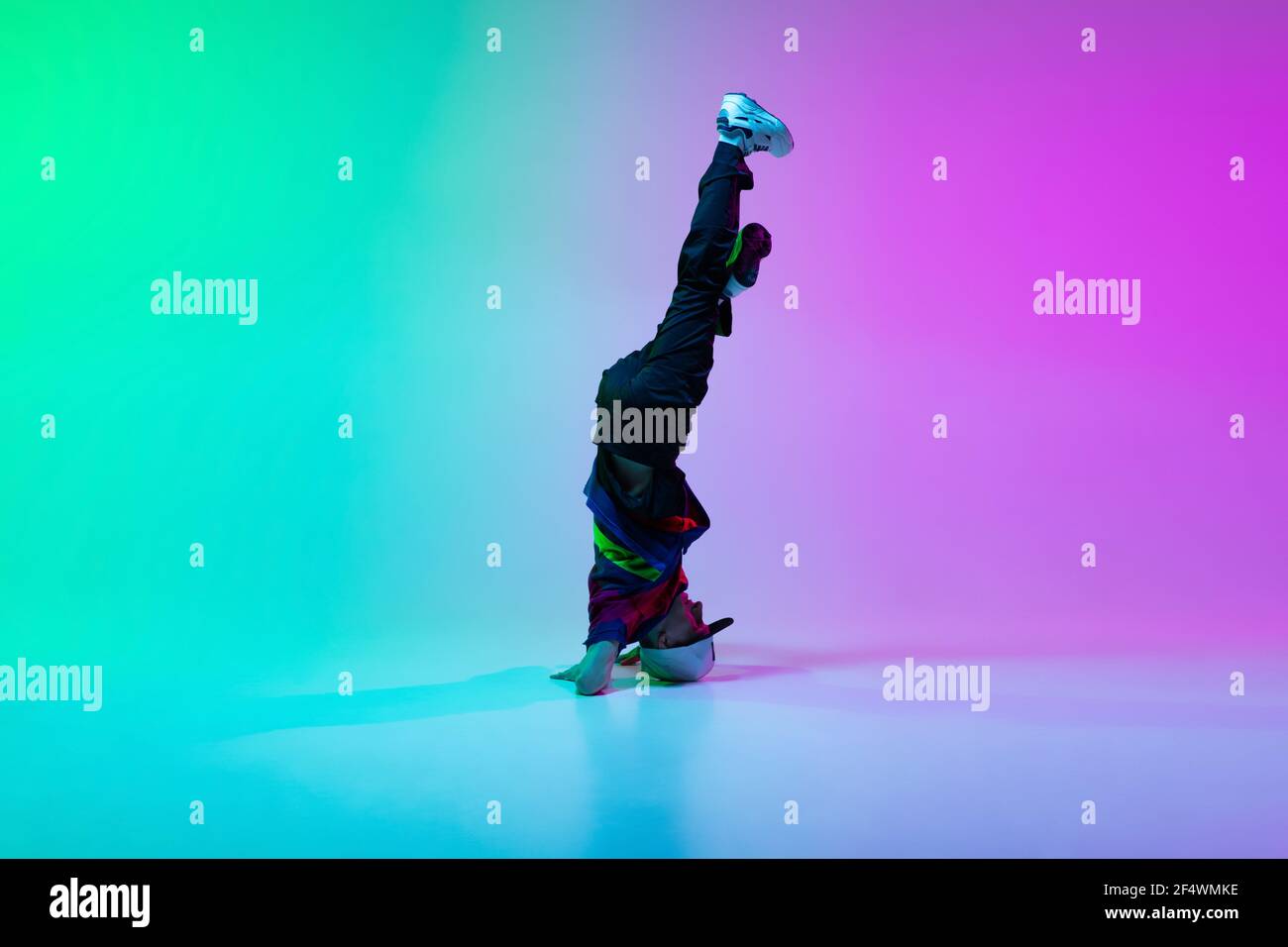 Bel ragazzo sportivo che balla hip-hop in abiti eleganti su sfondo sfumato colorato nella sala da ballo in luce al neon. Foto Stock