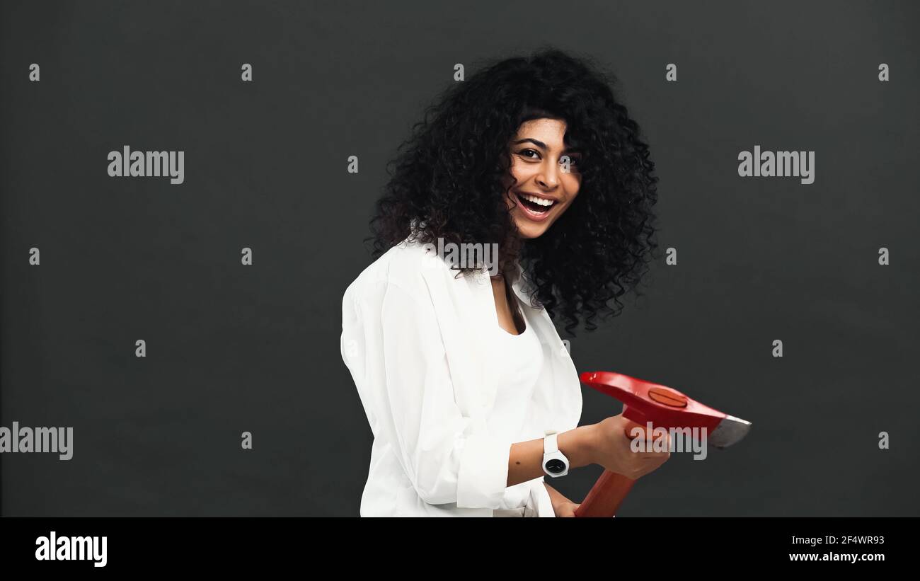 Sorridente donna ispanica che tiene l'ascia isolata su nero Foto Stock