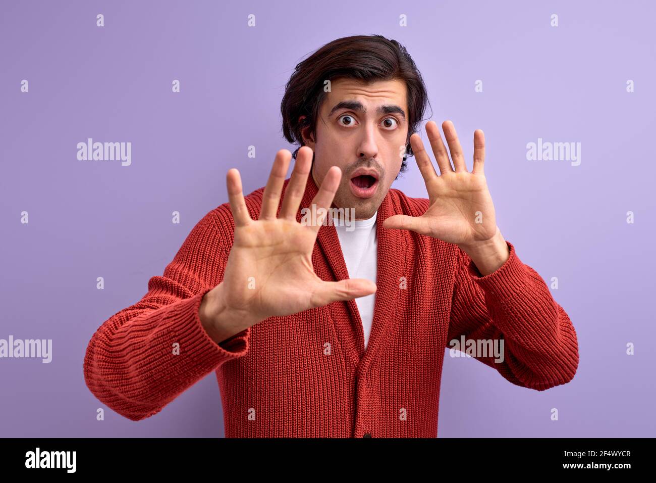 Paura giovane uomo in difesa atteggiamento gesturing stop con le mani, isolato su sfondo viola, dire no, shwoing palmo a macchina fotografica, spaventato e spaventato Foto Stock