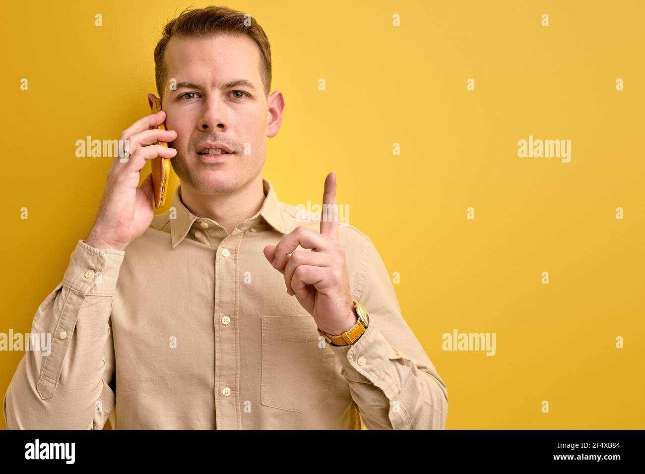 Ne ho idea. Uomo che condivide idee con il partner commerciale mentre si parla al telefono, stare pensando alla domanda, isolato su sfondo giallo Foto Stock