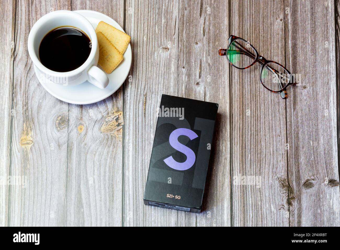 La scatola di un telefono cellulare Samsung Galaxy S21 o. telefono delle cellule posato su un tavolo di legno vicino ad a. caffè e bicchieri Foto Stock