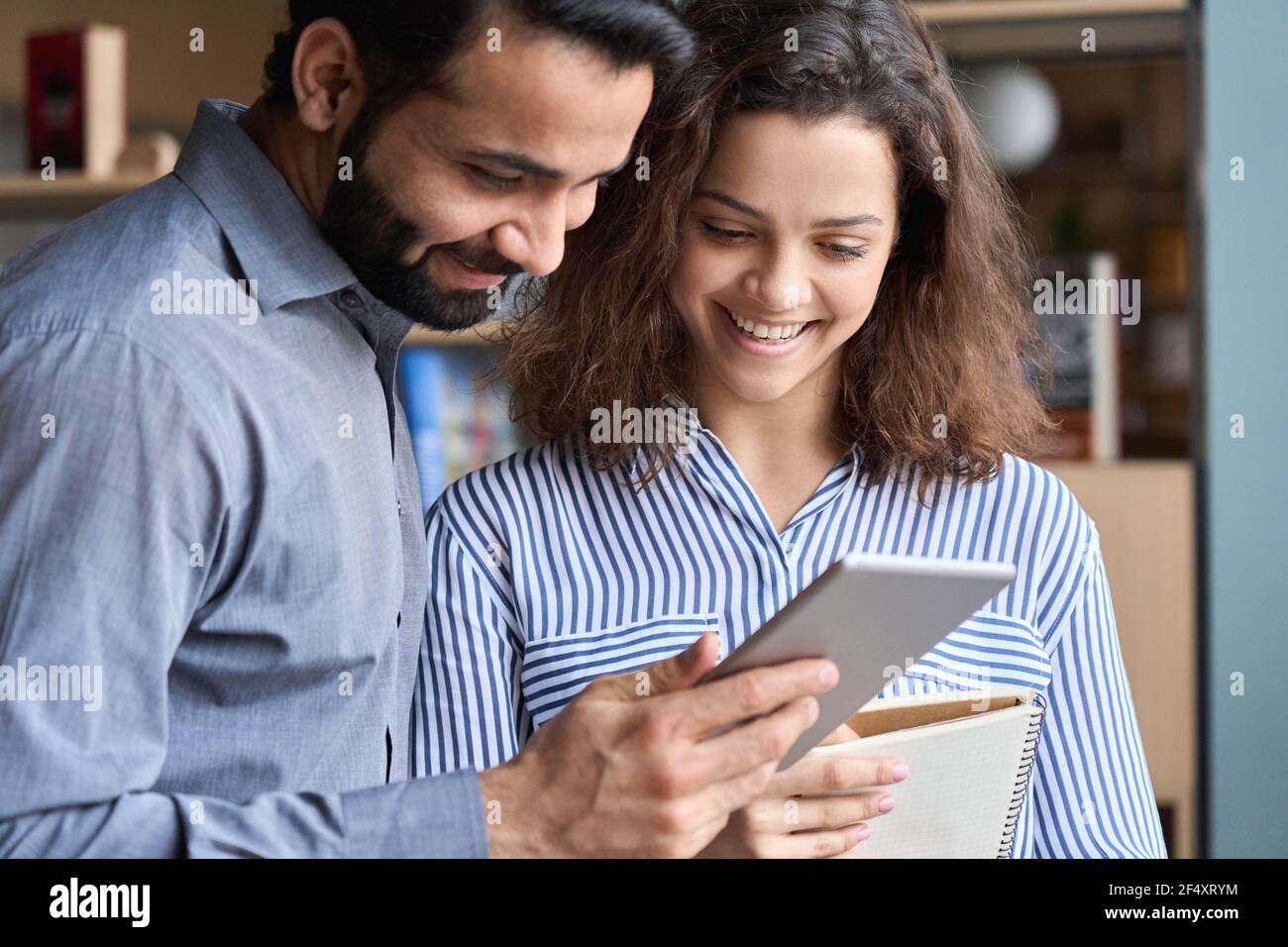 Sorridenti colleghi indiani e latini che parlano utilizzando il tablet digitale in ufficio. Foto Stock