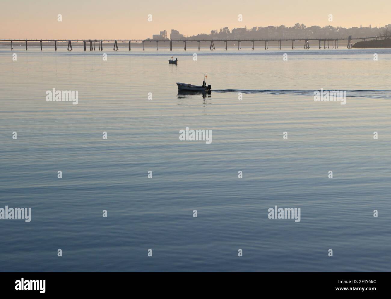 Una piccola barca da pesca che si dirige verso la baia di Santander Cantabria Spagna con il molo di gas di petrolio liquido dietro la primavera del sole della mattina presto Foto Stock