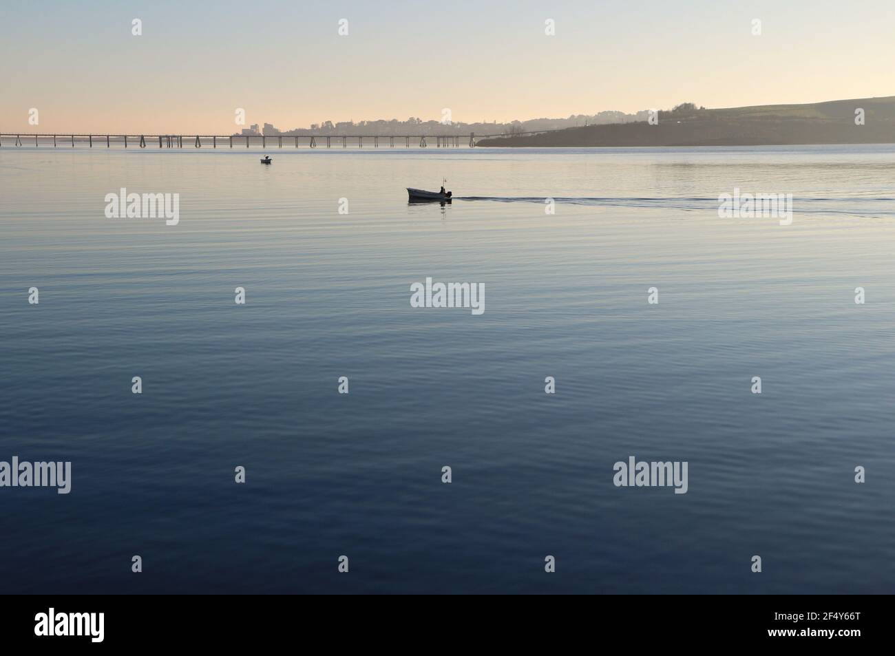 Una piccola barca da pesca che si dirige verso la baia di Santander Cantabria Spagna con il molo di gas di petrolio liquido dietro la primavera del sole della mattina presto Foto Stock