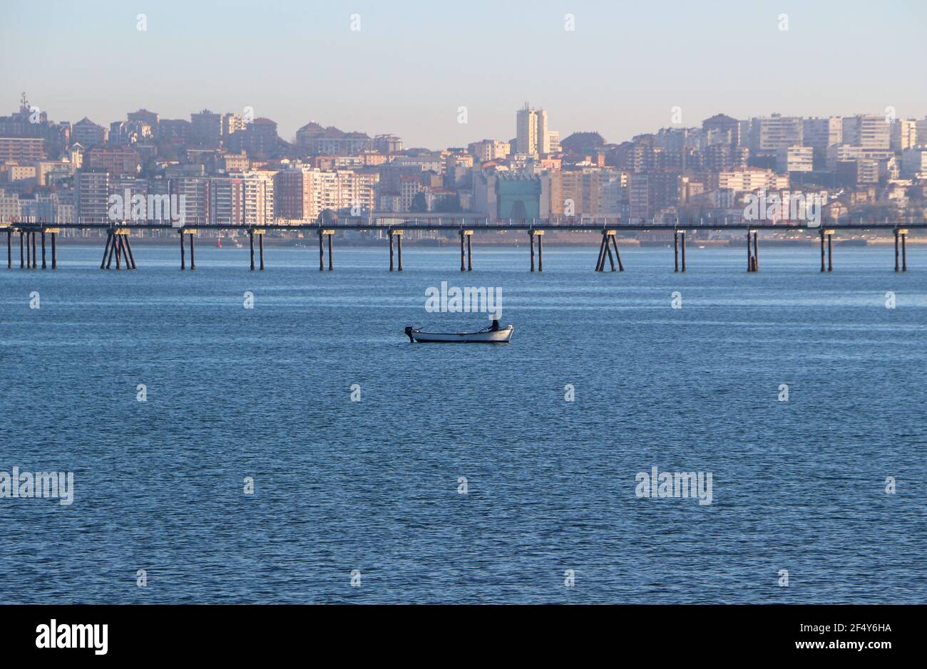 Una piccola barca da pesca nella baia di Santander Cantabria Spagna con la città alle spalle e il molo di gas di petrolio liquido primo mattino sole Foto Stock