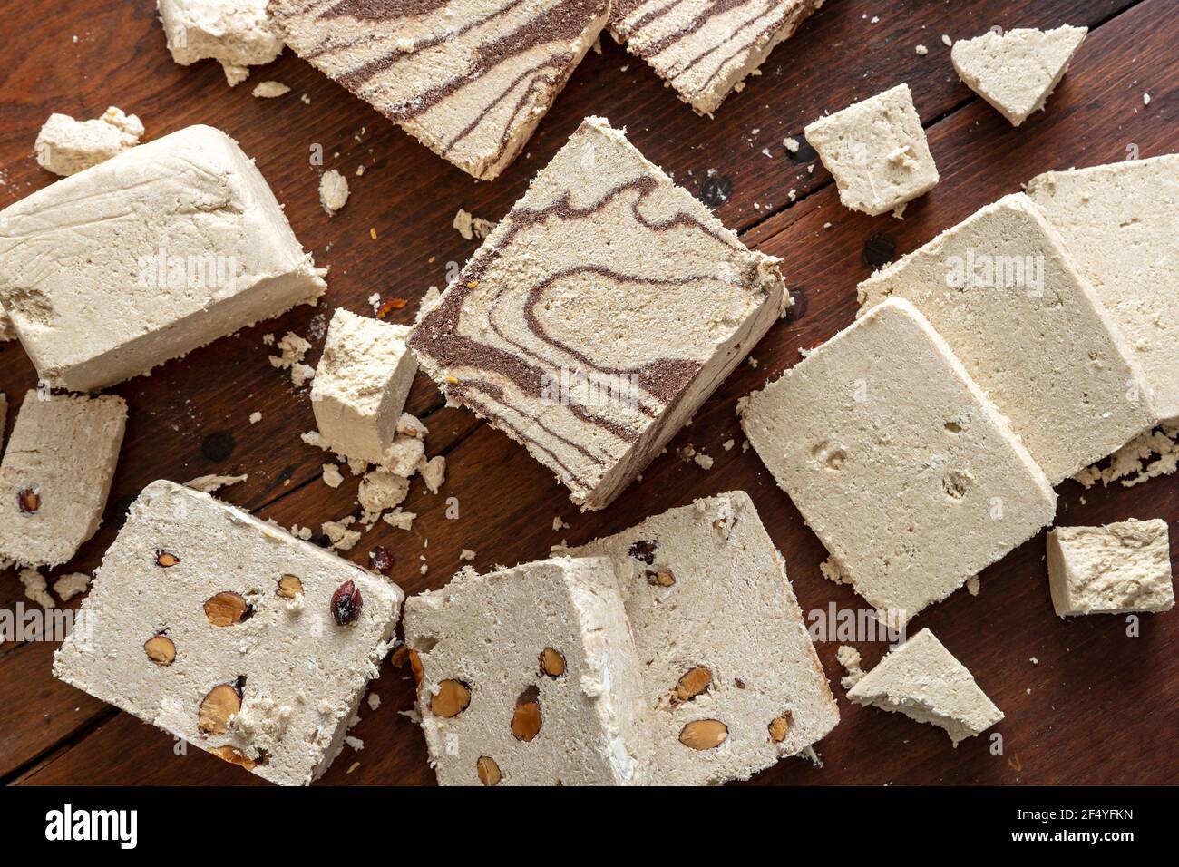 Halva varietà cacao e mandorle piatto adagiato su sfondo tavola di legno. Halvah alla vaniglia o pezzi di halwa con noci e cioccolato. Tradizionale dolce confe Foto Stock