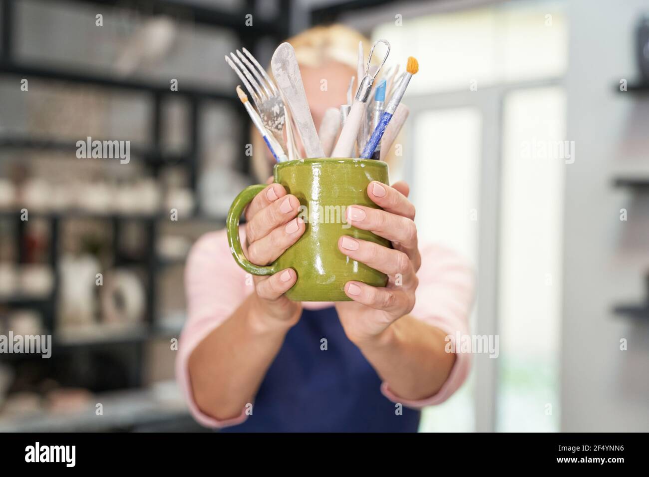Cose necessarie. Primo piano di mani di donne che tengono gli attrezzi, spazzole per la creazione di ceramica creta artigianale ciotola in laboratorio di ceramica Foto Stock