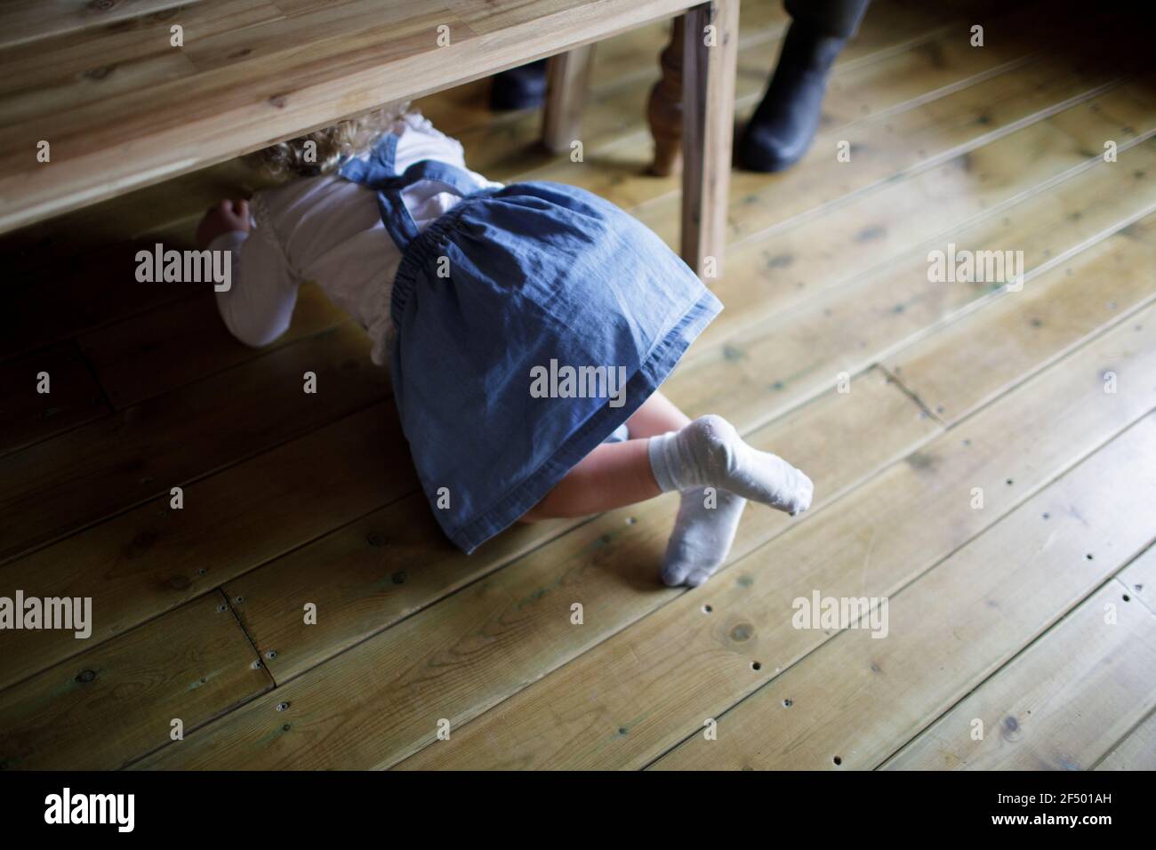 Ragazza carina in denim vestito strisciando sotto la panca di legno da pranzo Foto Stock