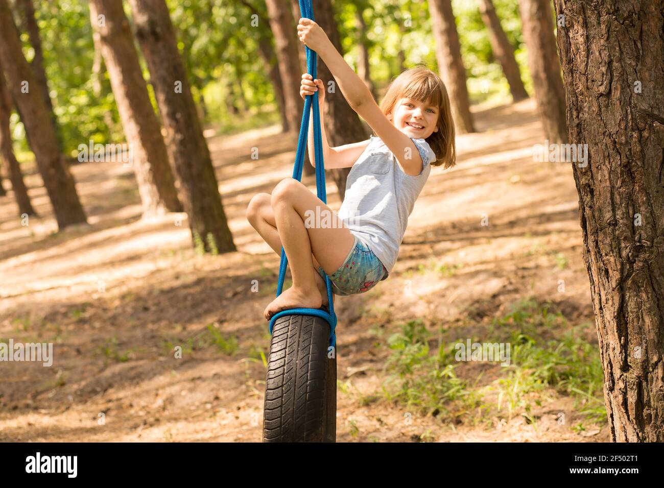 Carino bambina che oscilla sulla ruota attaccata al grande albero nella foresta di autunno. Foto Stock