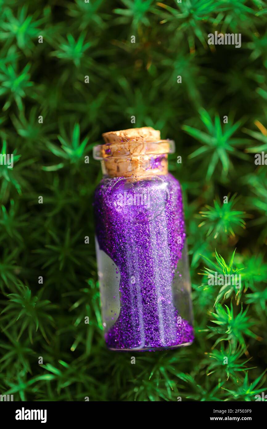 Magic Potion.Bottle con liquido luccicante viola in muschio verde su sfondo verde sfocato foresta.concetto di magia e fiabe. Foto Stock