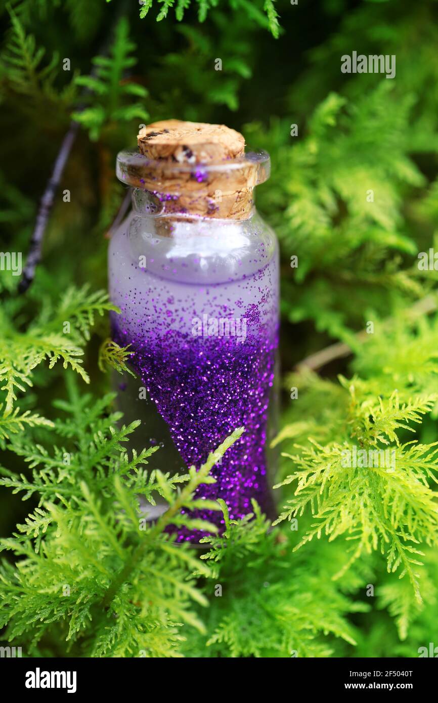 Magic Potion.Bottle con liquido viola scintillante in muschio verde su sfondo verde sfocato foresta.concetto di magia e favole. Foto Stock